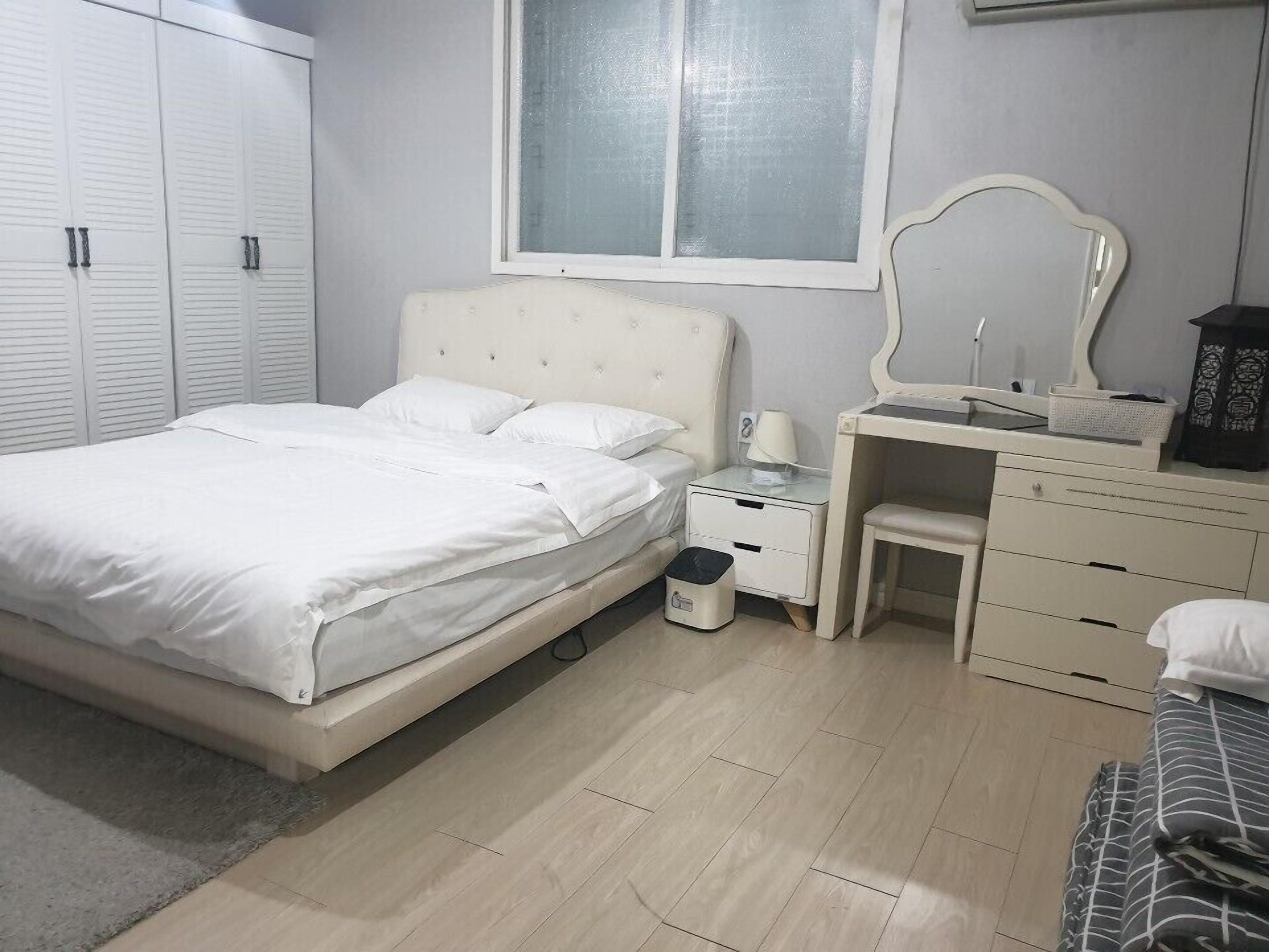 A bedroom with a bed, bedside table, dresser, and a window.