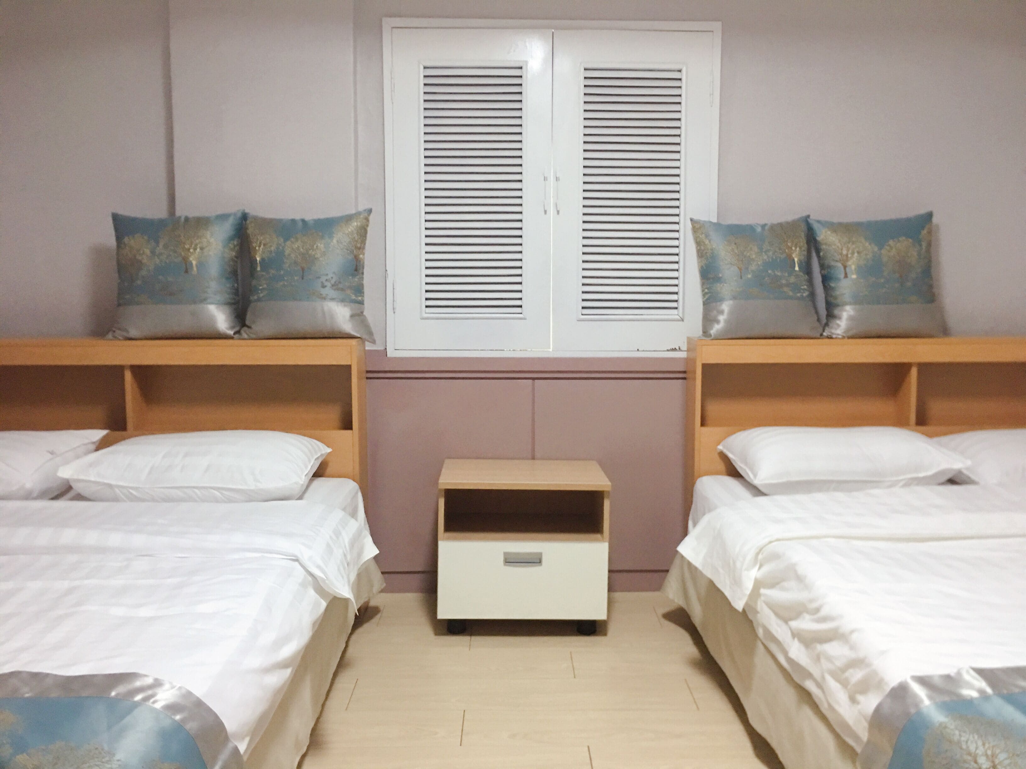 A room with two single beds, a small bedside table, and a window with shutters.
