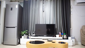 A modern living room with a flat-screen TV, a wooden coffee table, a refrigerator, and a sofa.