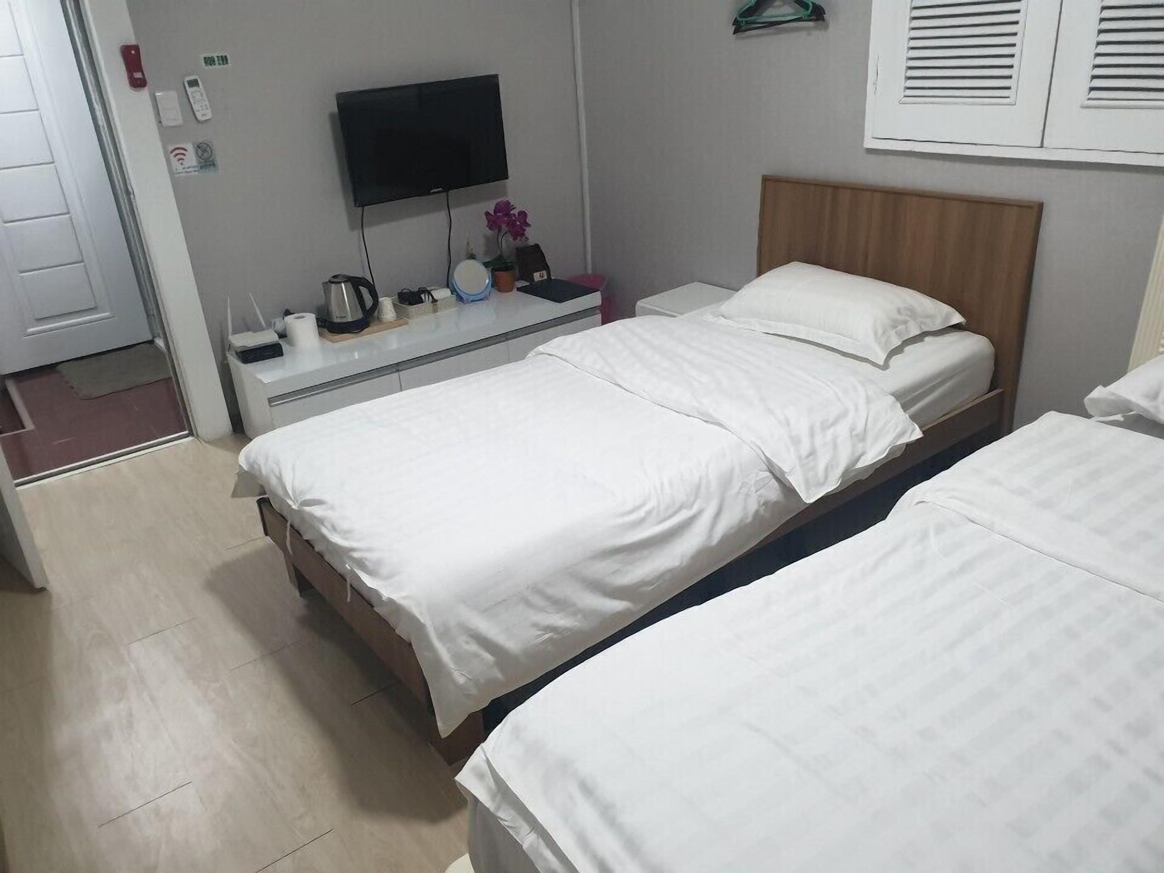 A hotel room with a bed, bedside table, TV, and a wall-mounted heater.