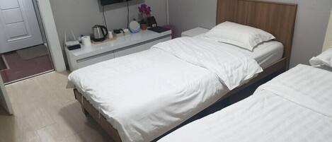 A hotel room with a bed, bedside table, TV, and a wall-mounted heater.