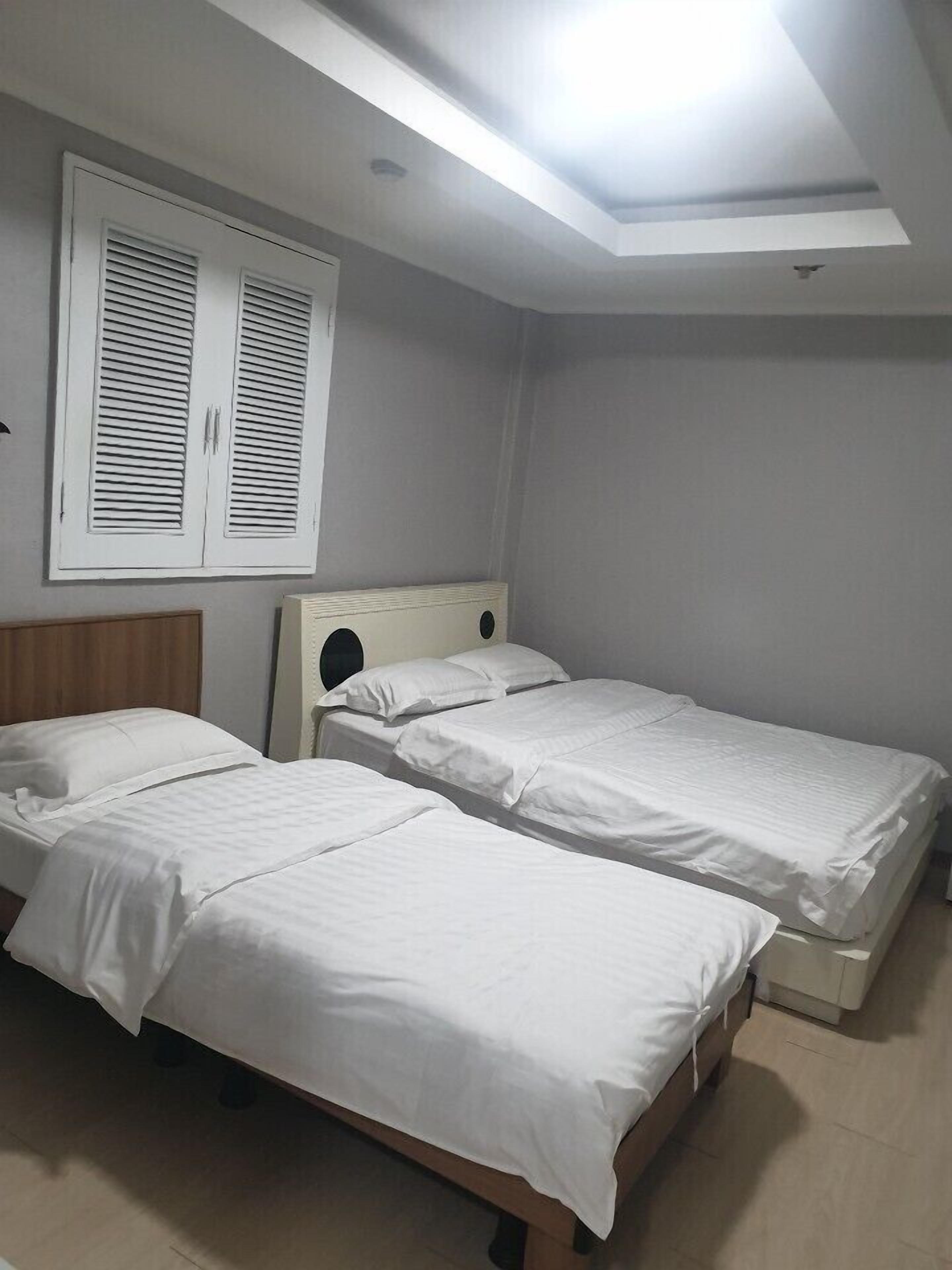 A room with two single beds, a wooden headboard, a window with shutters, and a skylight.
