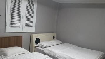 A room with two single beds, a wooden headboard, a window with shutters, and a skylight.