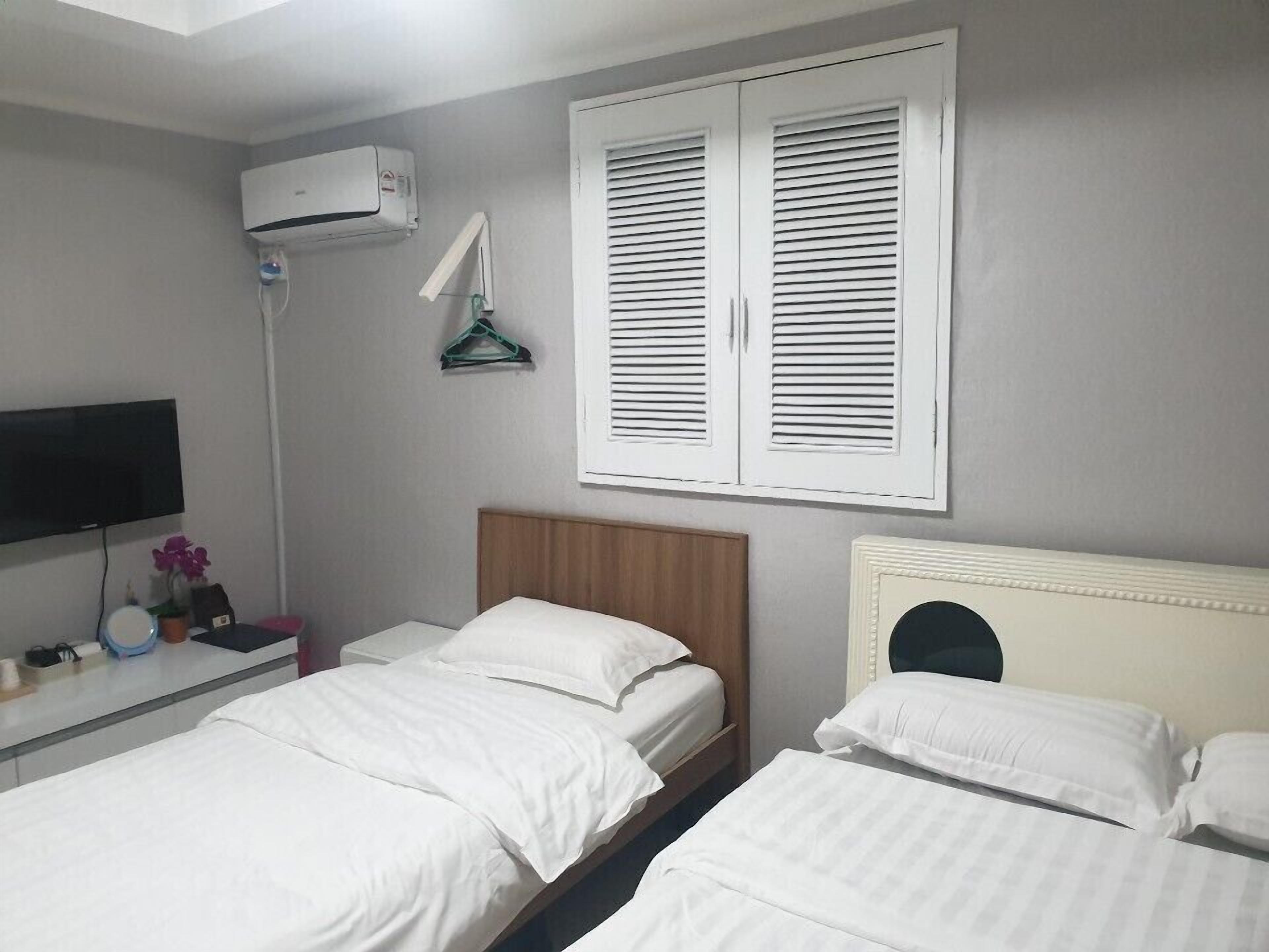 Una habitación de hotel con dos camas, televisión, aire acondicionado y una ventana con persianas.