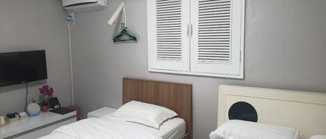 Una habitación de hotel con dos camas, televisión, aire acondicionado y una ventana con persianas.