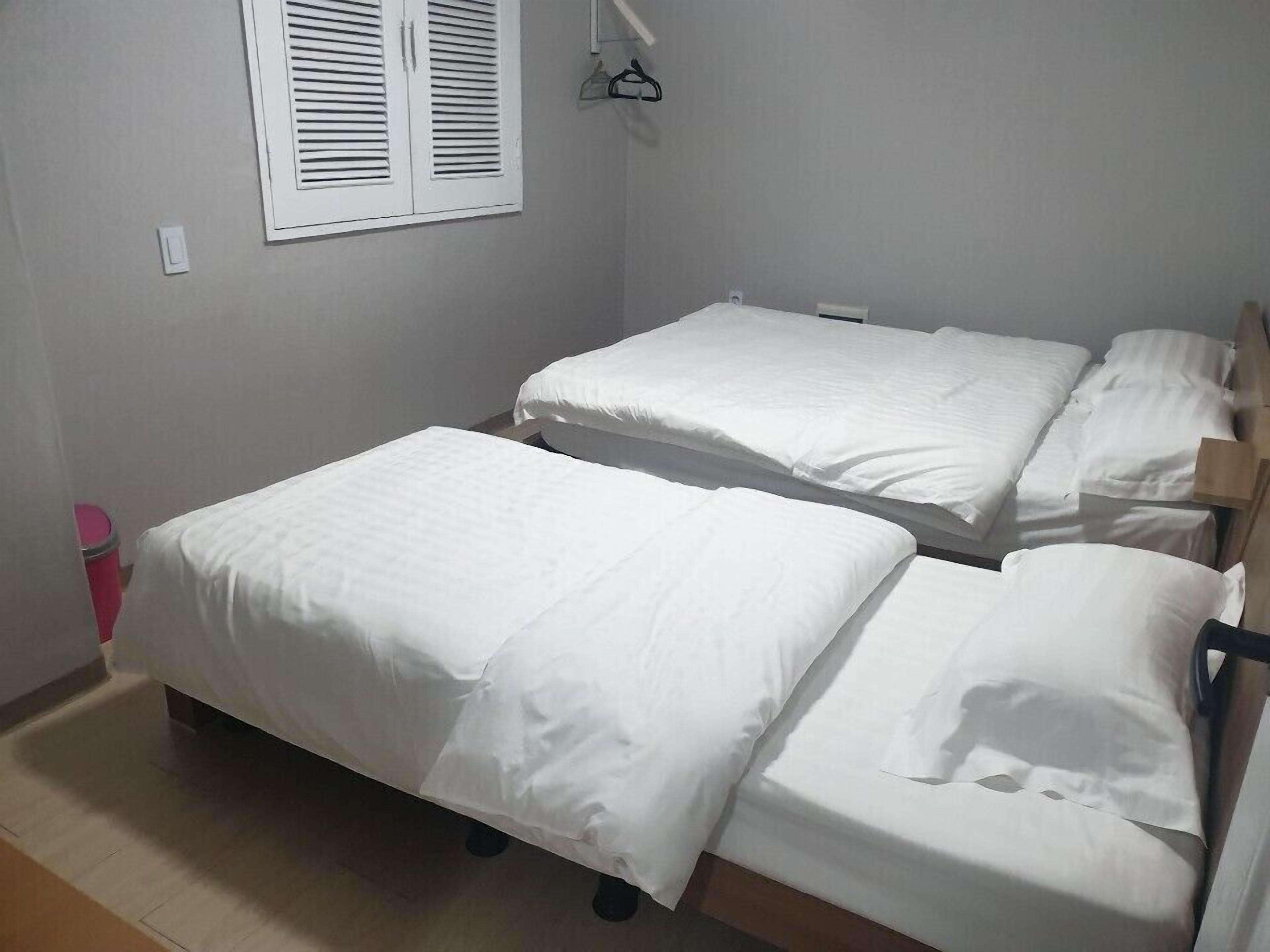 Een kleine, schone kamer met twee eenpersoonsbedden, een raam met witte luiken en een houten vloer.