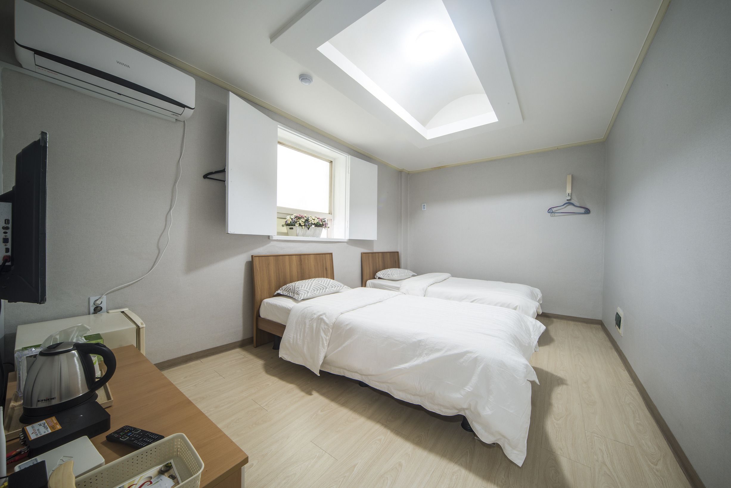 A hotel room with two beds, a desk with a kettle, a TV, and a skylight.