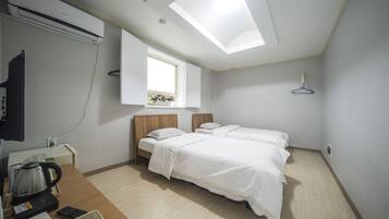 A hotel room with two beds, a desk with a kettle, a TV, and a skylight.