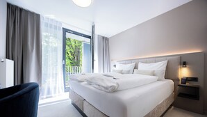 A modern hotel room with a large bed, a chair, a bedside table, and a view of the outdoors. - Digital Hotel Kronjuwel by BRIGHT Waldkirch - Self Check-in (Waldkirch)