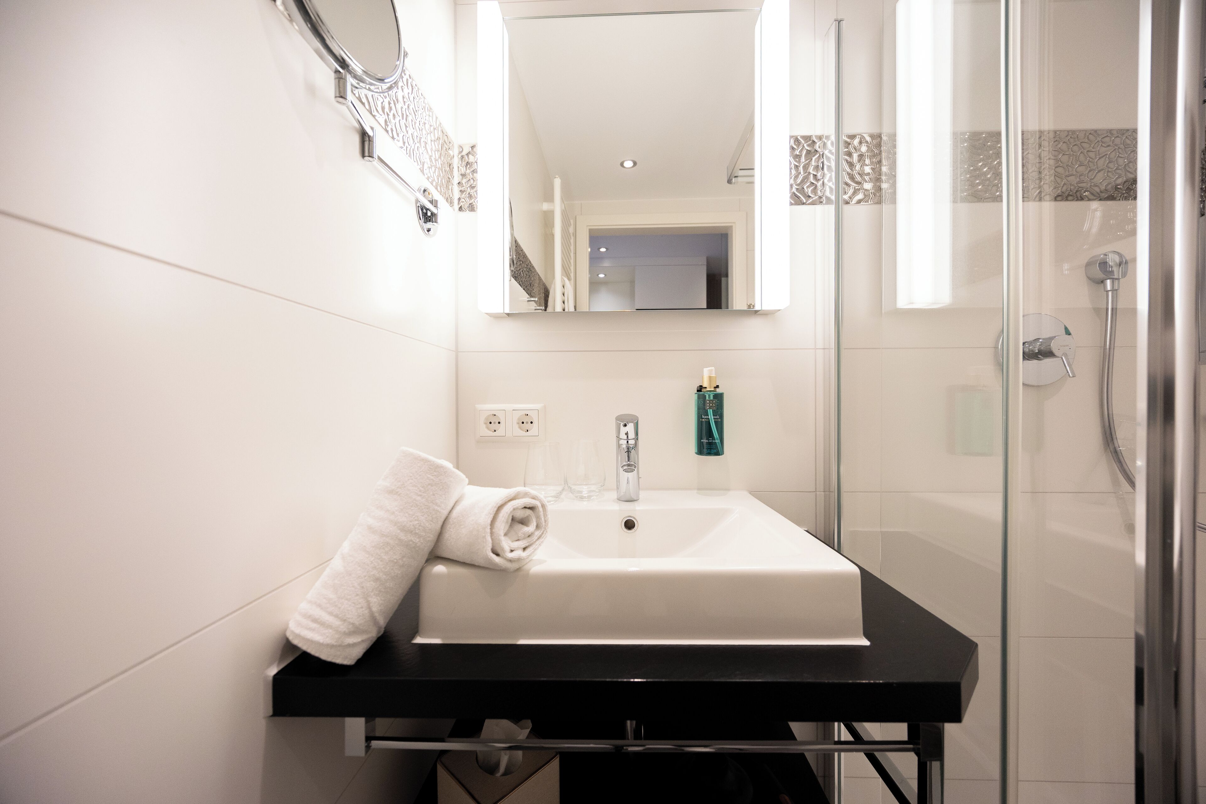 Un baño con lavamanos blanco, una toalla, un espejo y un box de ducha de vidrio.