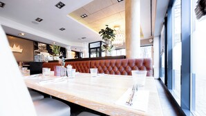 A restaurant with a long marble table, cushioned seating, and a large window offering a view. - Digital Hotel Kronjuwel by BRIGHT Waldkirch - Self Check-in (Waldkirch)