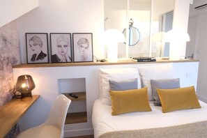 Ein modernes Schlafzimmer mit Bett, Nachttischlampen, einem Spiegel und Kunstwerken an der Wand.
