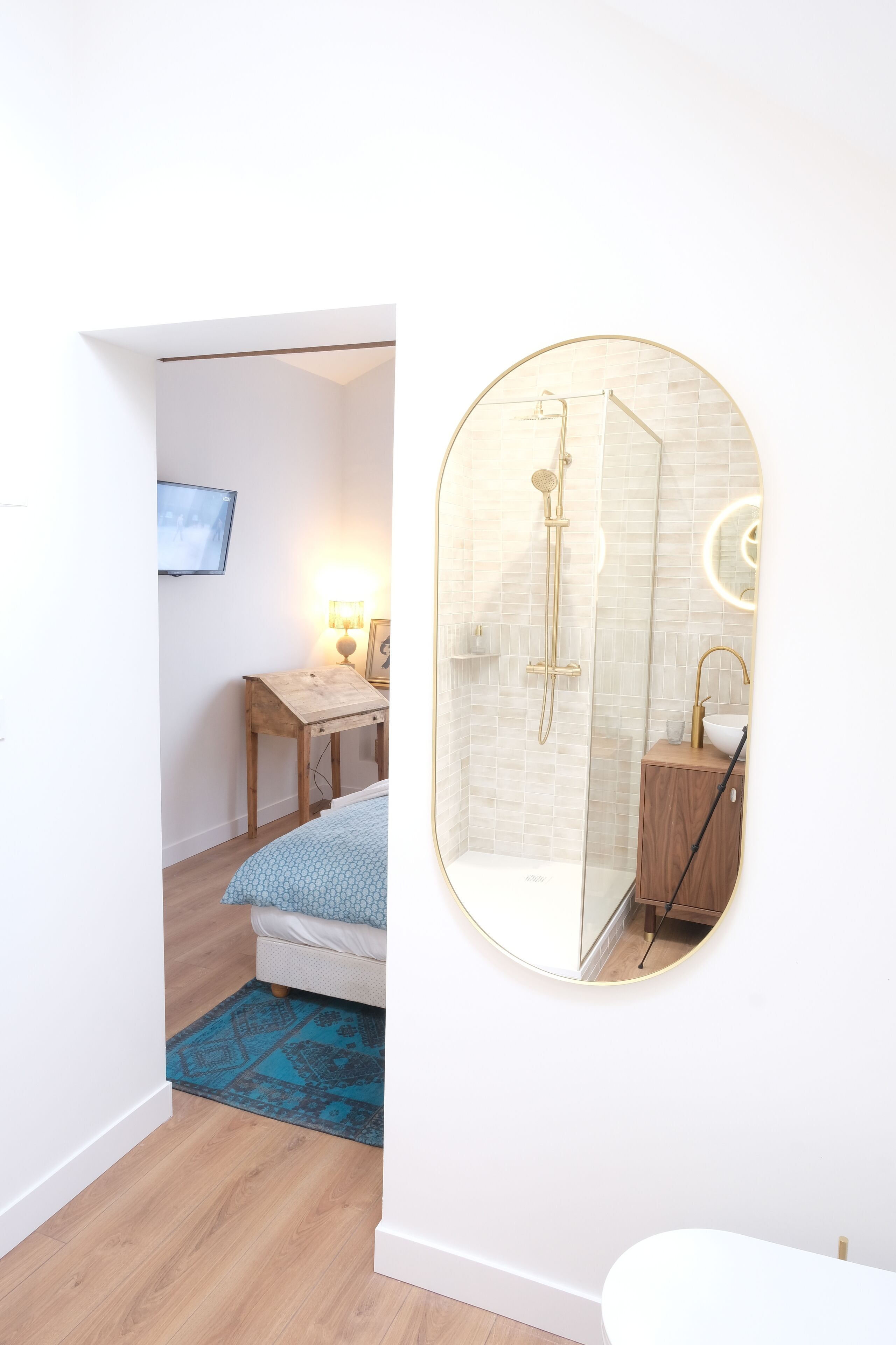 A modern bathroom with a glass-enclosed shower, a round mirror, and a wooden cabinet.