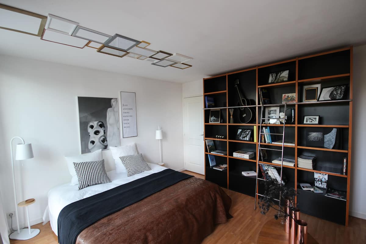 Un dormitorio moderno con una cama grande, una estantería y una lámpara de techo original.