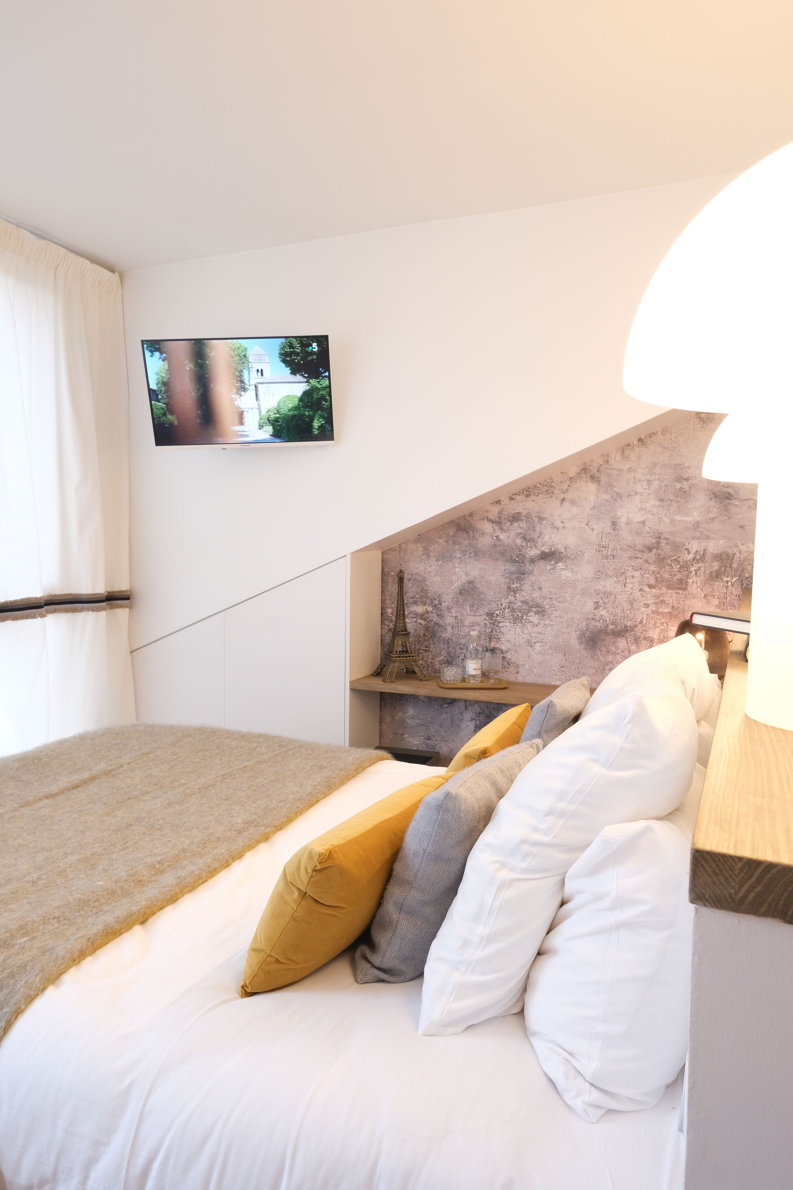 A bedroom with a bed, pillows, a TV, and a lamp.
