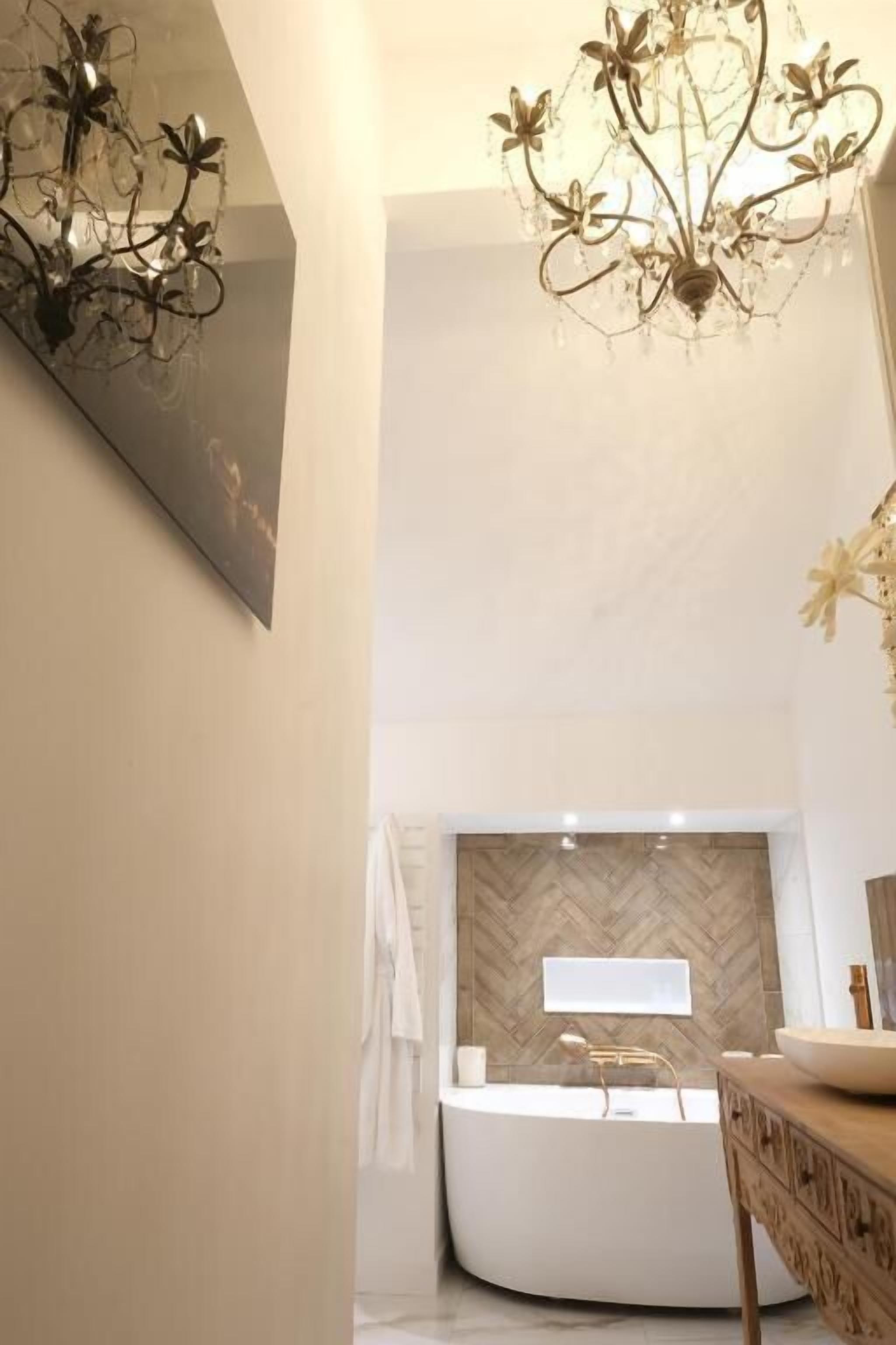 A modern bathroom with a freestanding bathtub, a mirror, and a decorative chandelier.