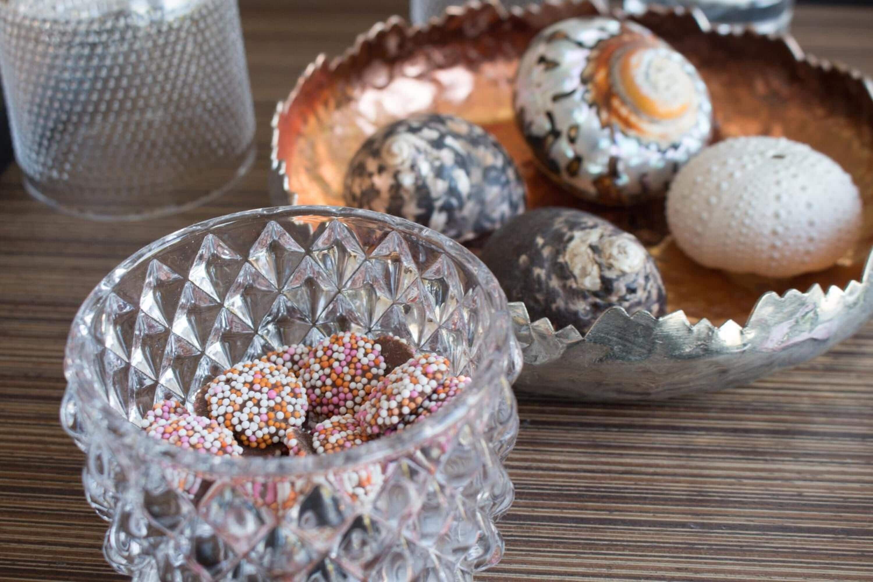 A clear glass bowl filled with colorful sprinkles and a metal bowl with various decorated cookies.