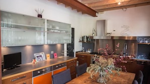 Une cuisine moderne avec des meubles en bois, un grand îlot central et un coin repas agrémenté d’un vase de fleurs séchées.