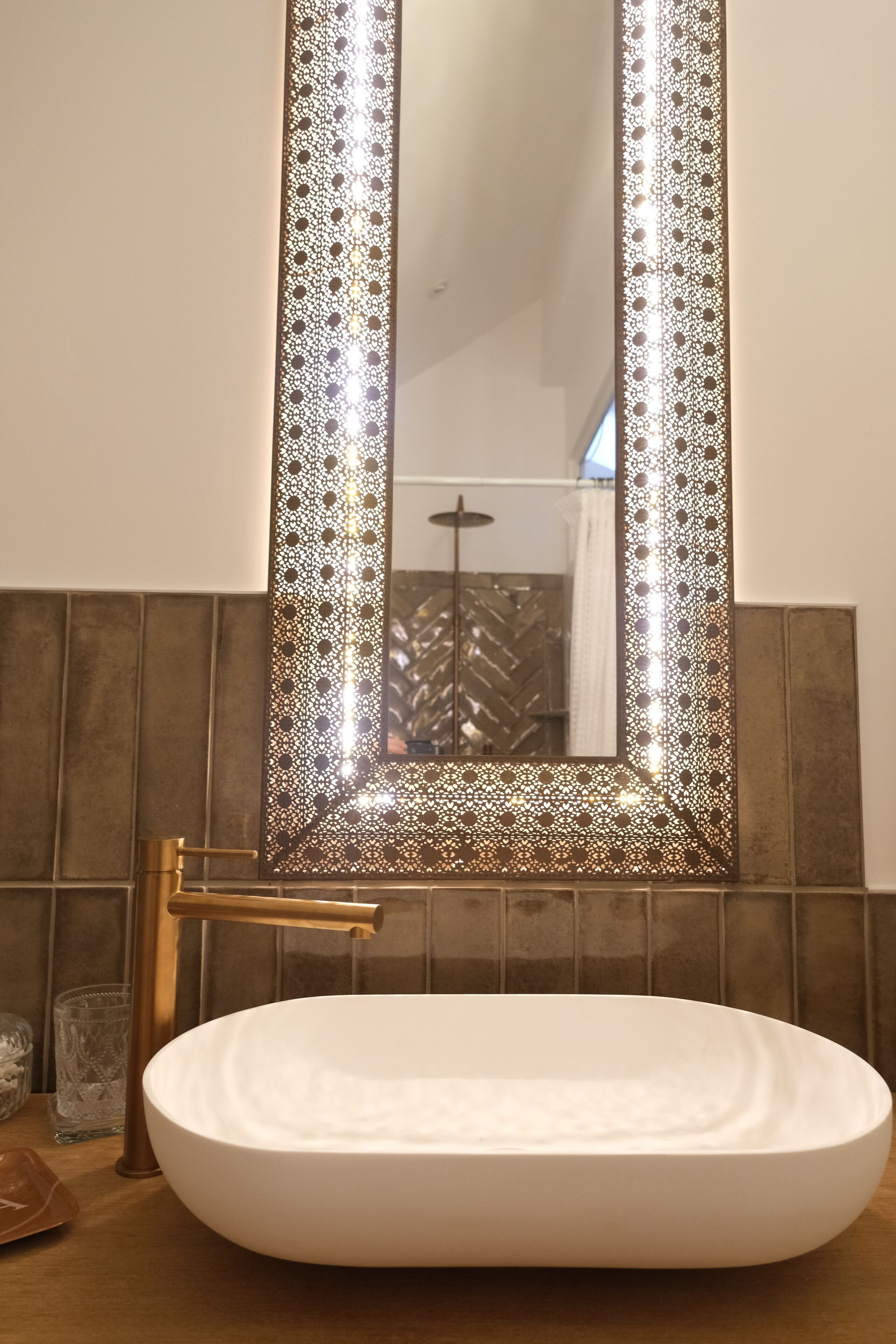 A bathroom with a white sink, a gold faucet, and a decorative mirror with a patterned frame.