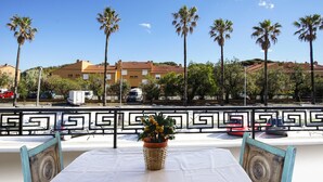 Una mesa con un centro de mesa de cesta tejida, barandilla de metal con diseño y vista a palmeras y edificios al fondo.