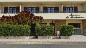 Un edificio de dos pisos con un balcón, un letrero que dice “Residence Les Mandariniers” y una planta grande con flores en la entrada.