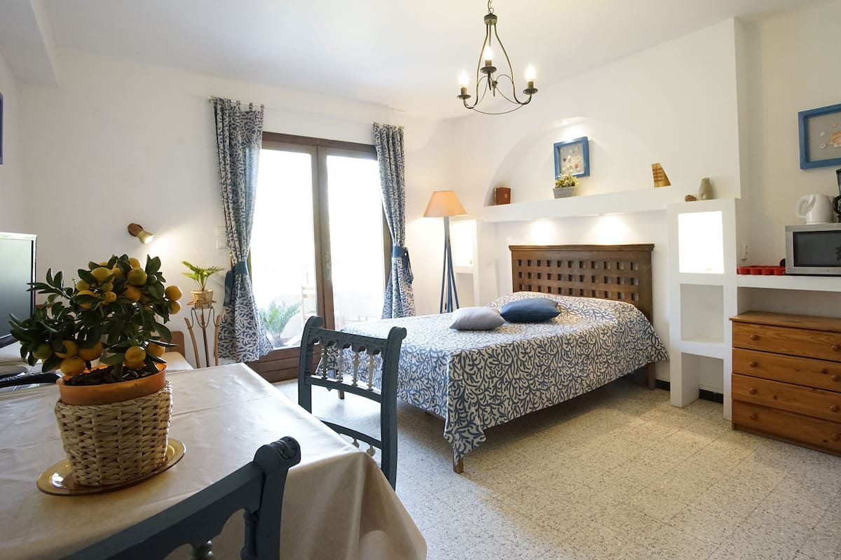 A bedroom with a bed, a desk, a chair, a lamp, a potted plant, a microwave, and a coffee maker.