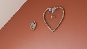 A neatly made bed with white linens and pillows, a wooden headboard, and two heart-shaped wall decorations. - Holiday Home 't Regulierenhuisje (Tongeren)