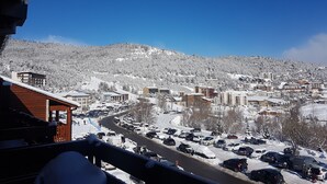 Un pueblo nevado en la montaña, con vista a una carretera bordeada de coches estacionados y edificios.