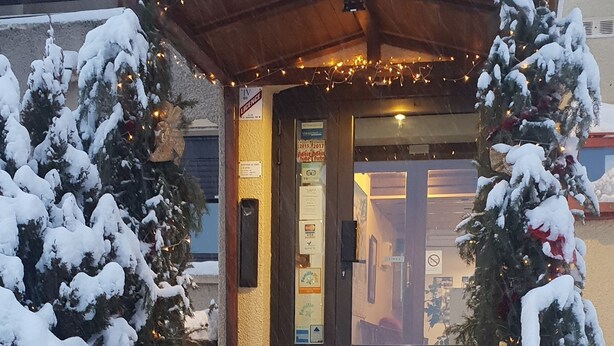 Una entrada nevada con un letrero que dice "ENTREE" y un árbol de Navidad decorado con luces.