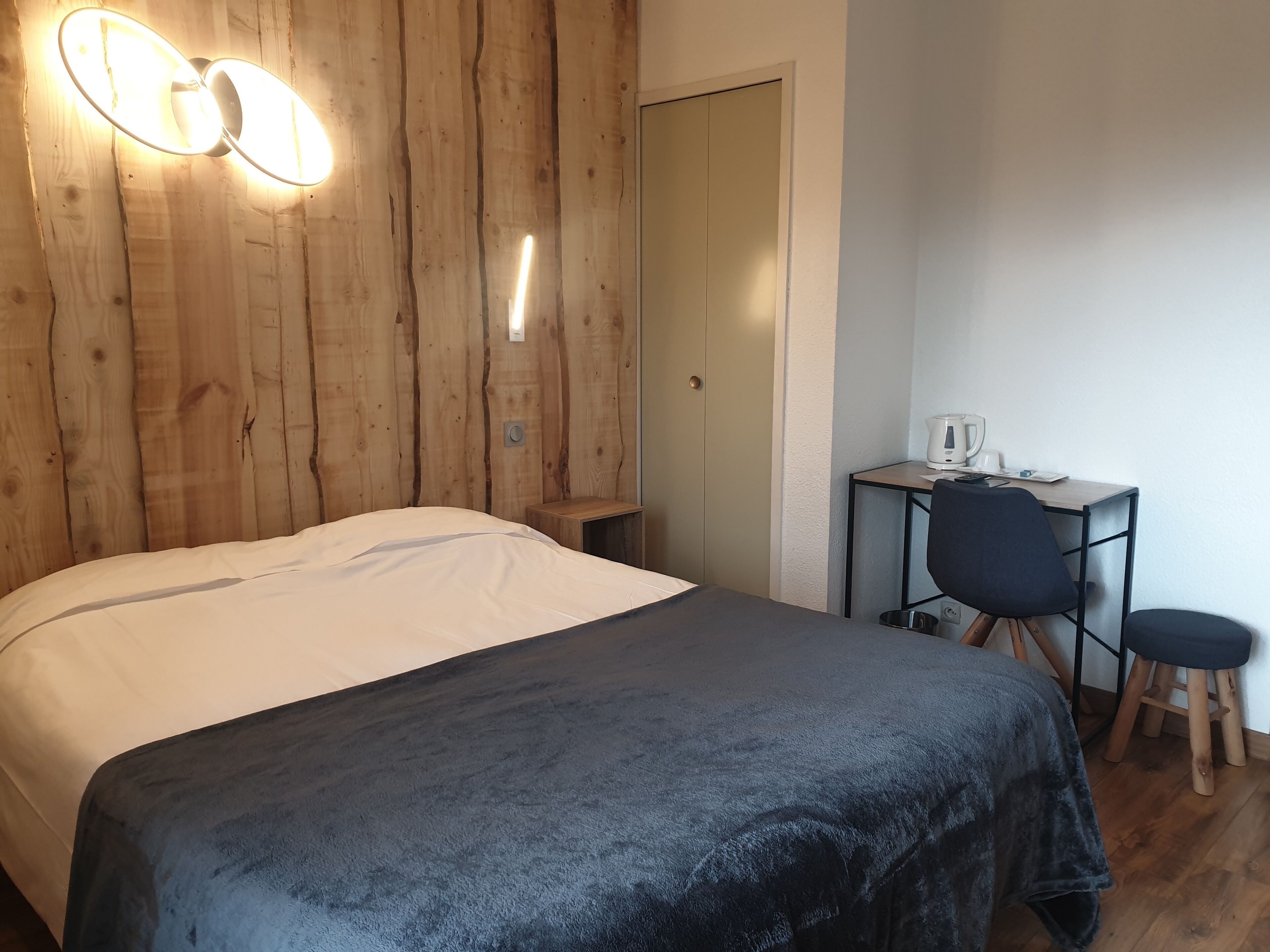 A room with a bed, a desk with a chair, and a wooden wall.