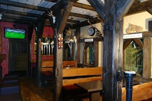 A rustic interior with wooden beams, benches, a television, and a sign that says "Enjoy the day with a smile." - Heidehotel Jagdhof Dobra GmbH (Bad Liebenwerda)
