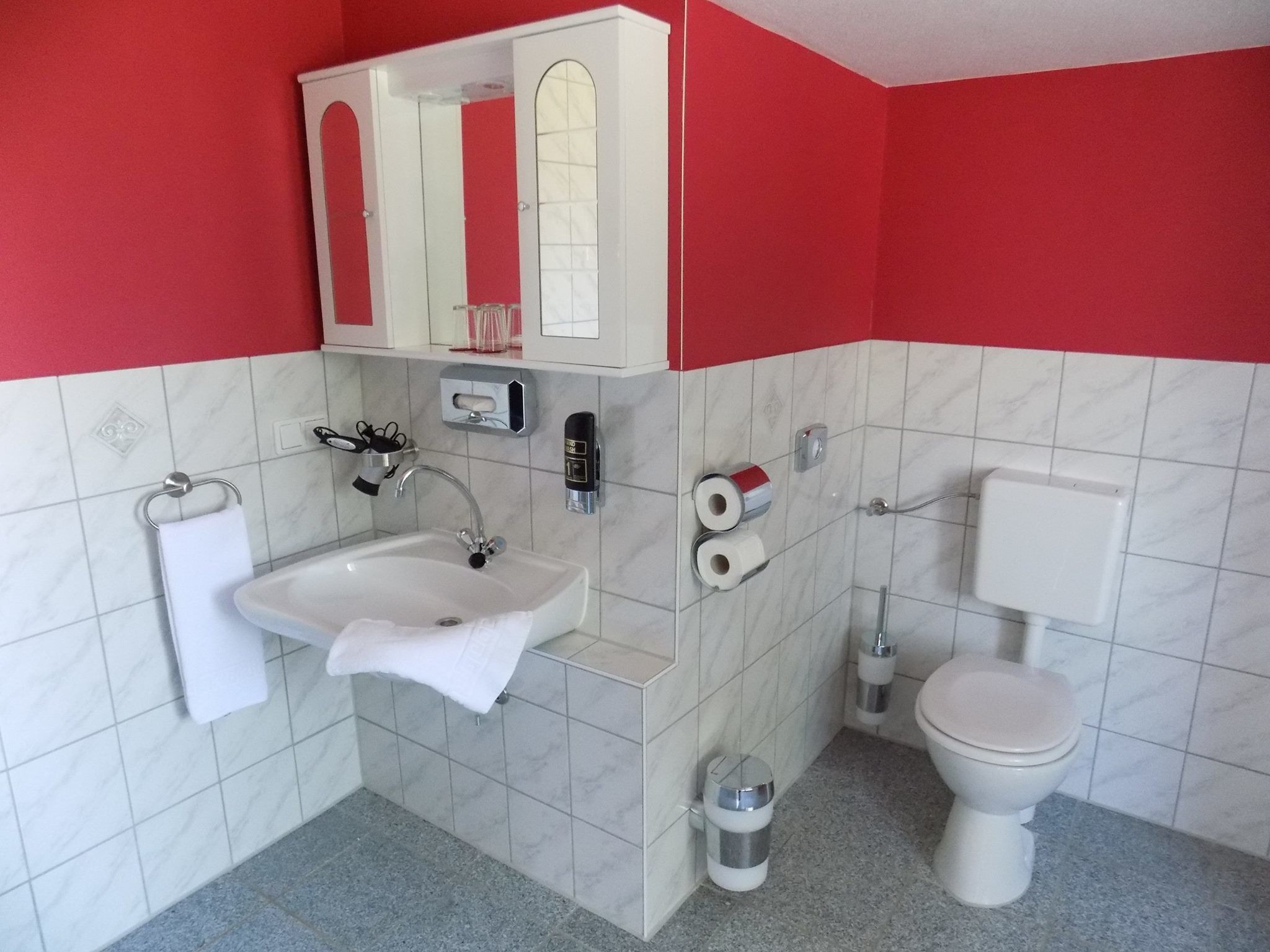 Un baño con lavamanos, espejo, inodoro y toallero.