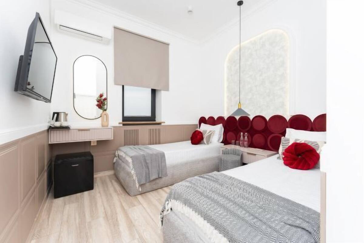 A hotel room with two beds, a desk, a mirror, a TV, and a wardrobe.