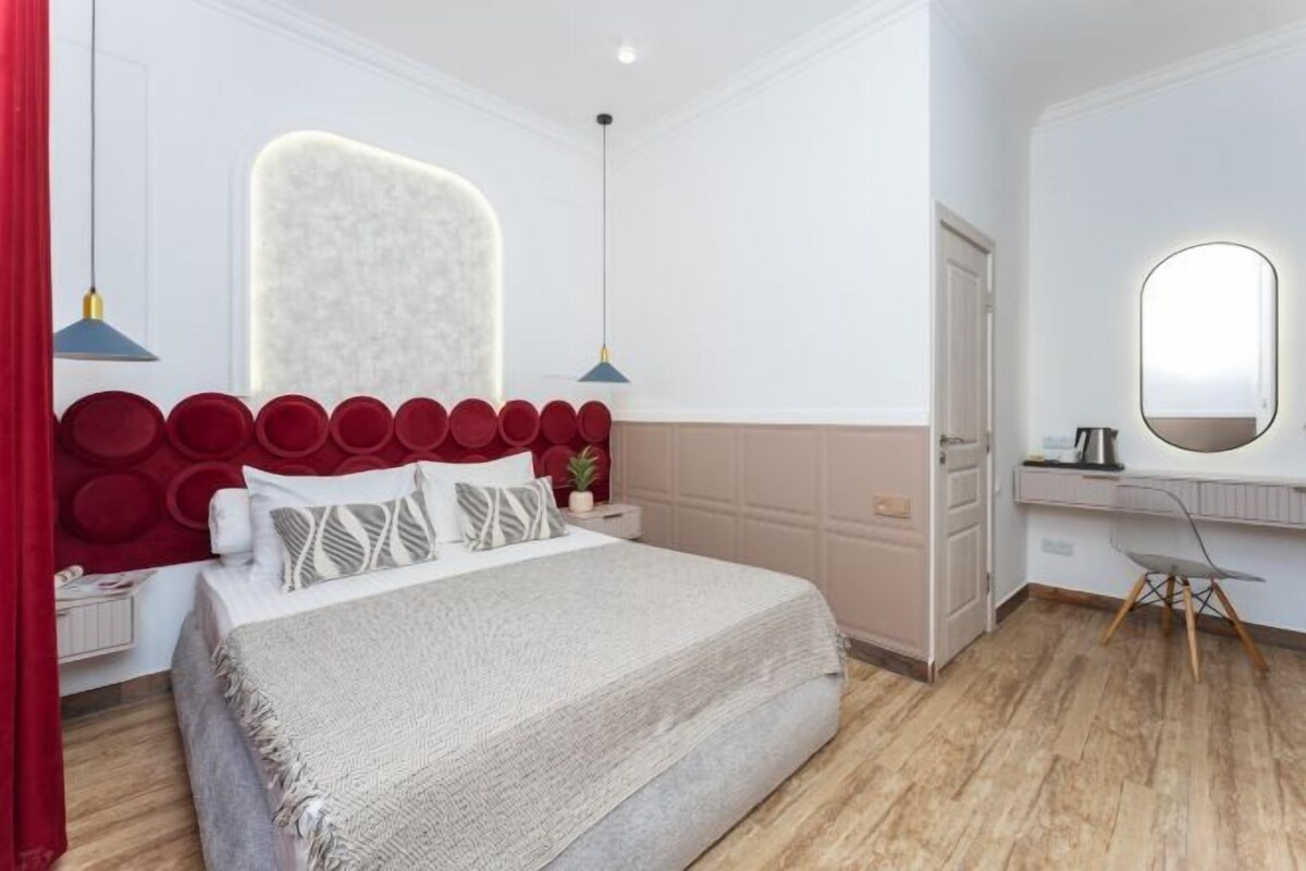 A modern bedroom with a large bed, a vanity with a mirror, and a desk.