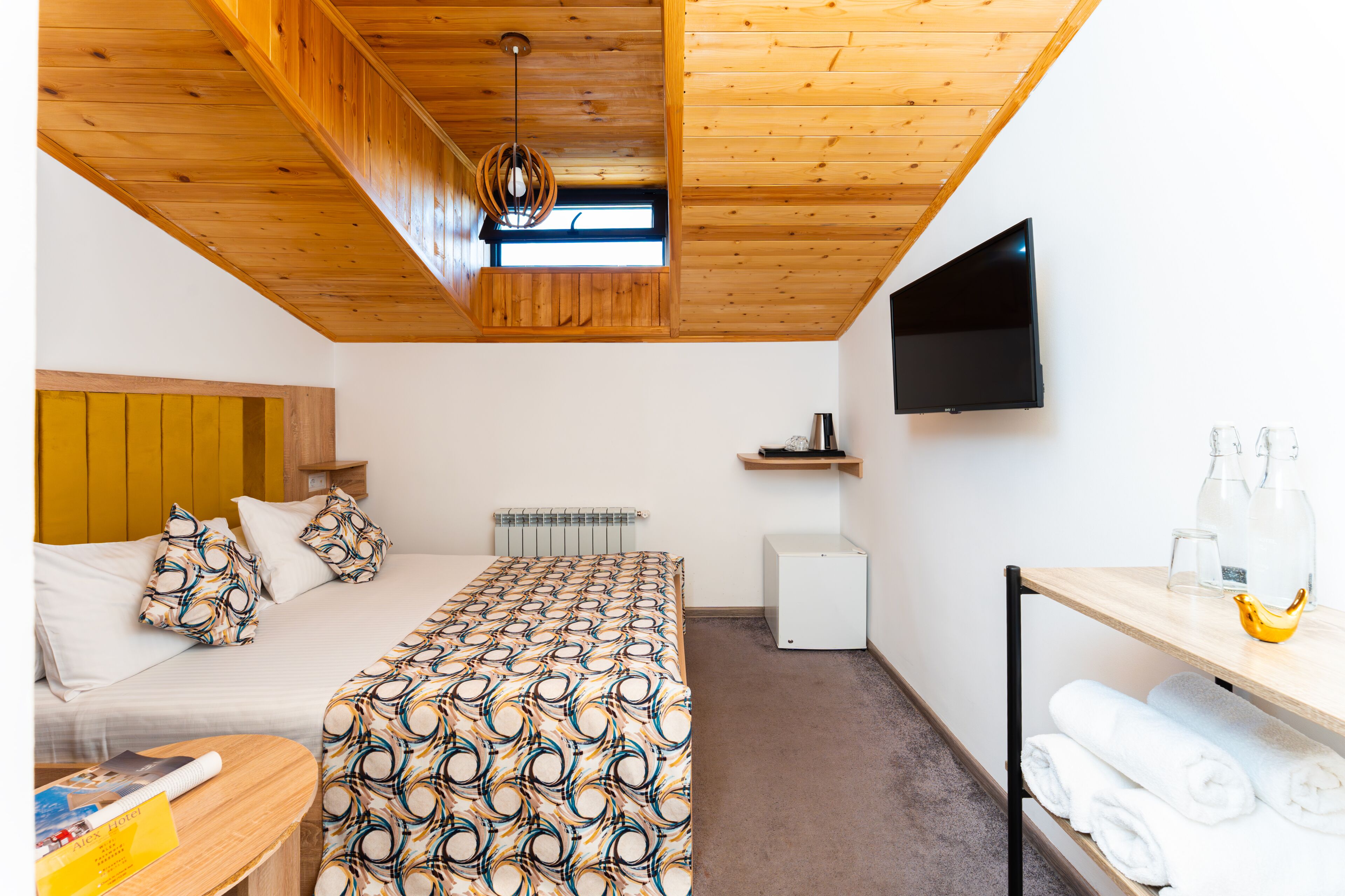 Een slaapkamer met een bed, een bureau, een televisie en een plank met flessen.