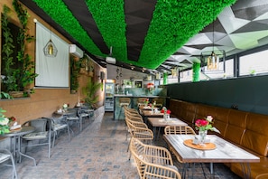 A restaurant with outdoor seating, green artificial foliage, wicker chairs, and a brick floor. - Alex Hotel (Yerevan)