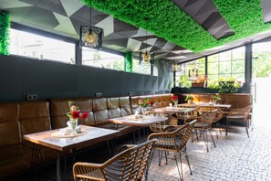 Un restaurante con pared verde, asientos de cuero y sillas de mimbre.