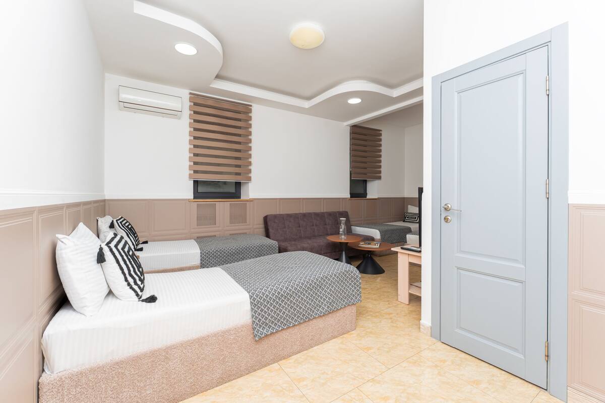 A hotel room with two beds, a sofa, a small table, and a door.