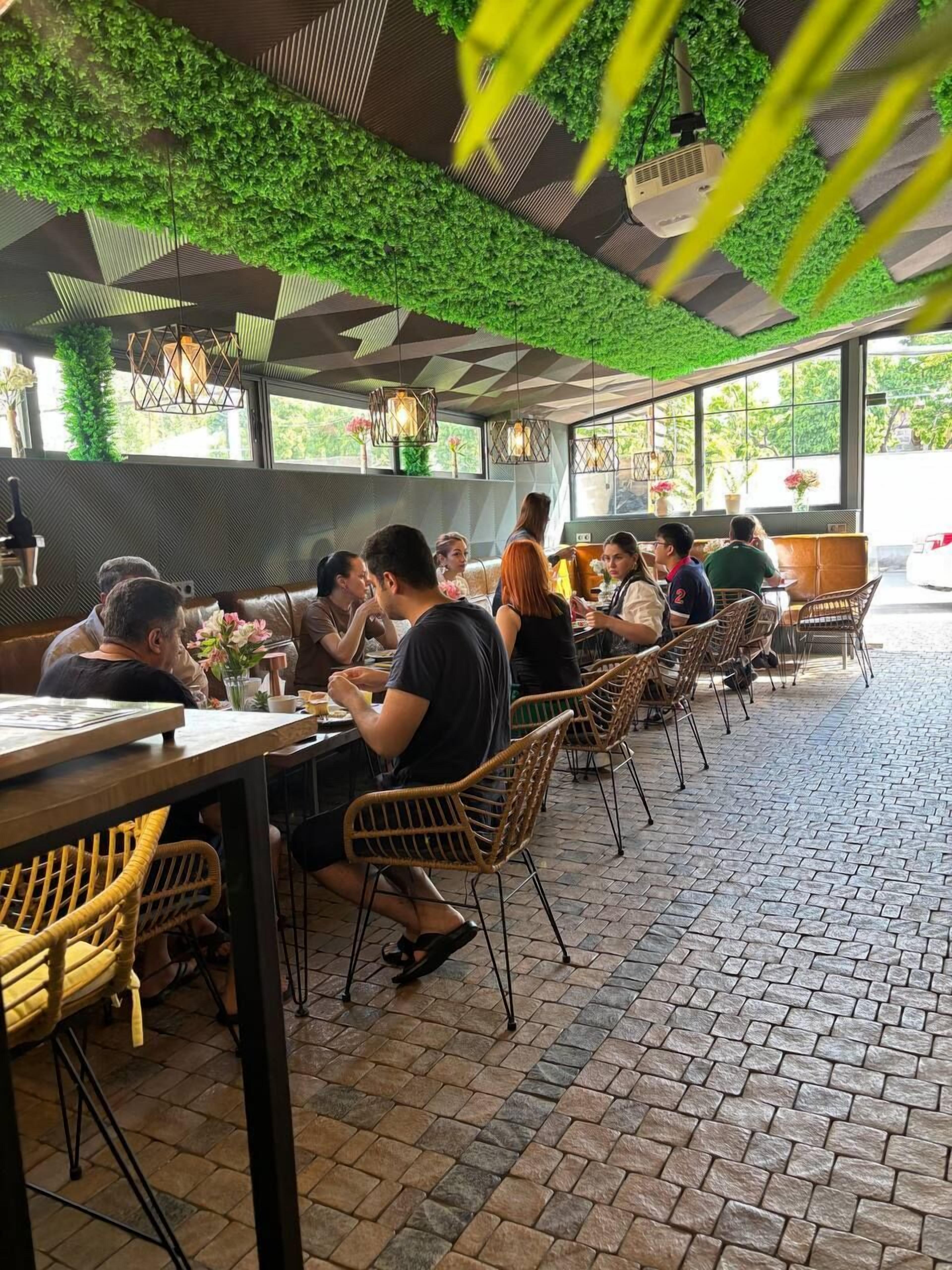 An outdoor dining area with brick flooring, wicker chairs, and green foliage overhead.