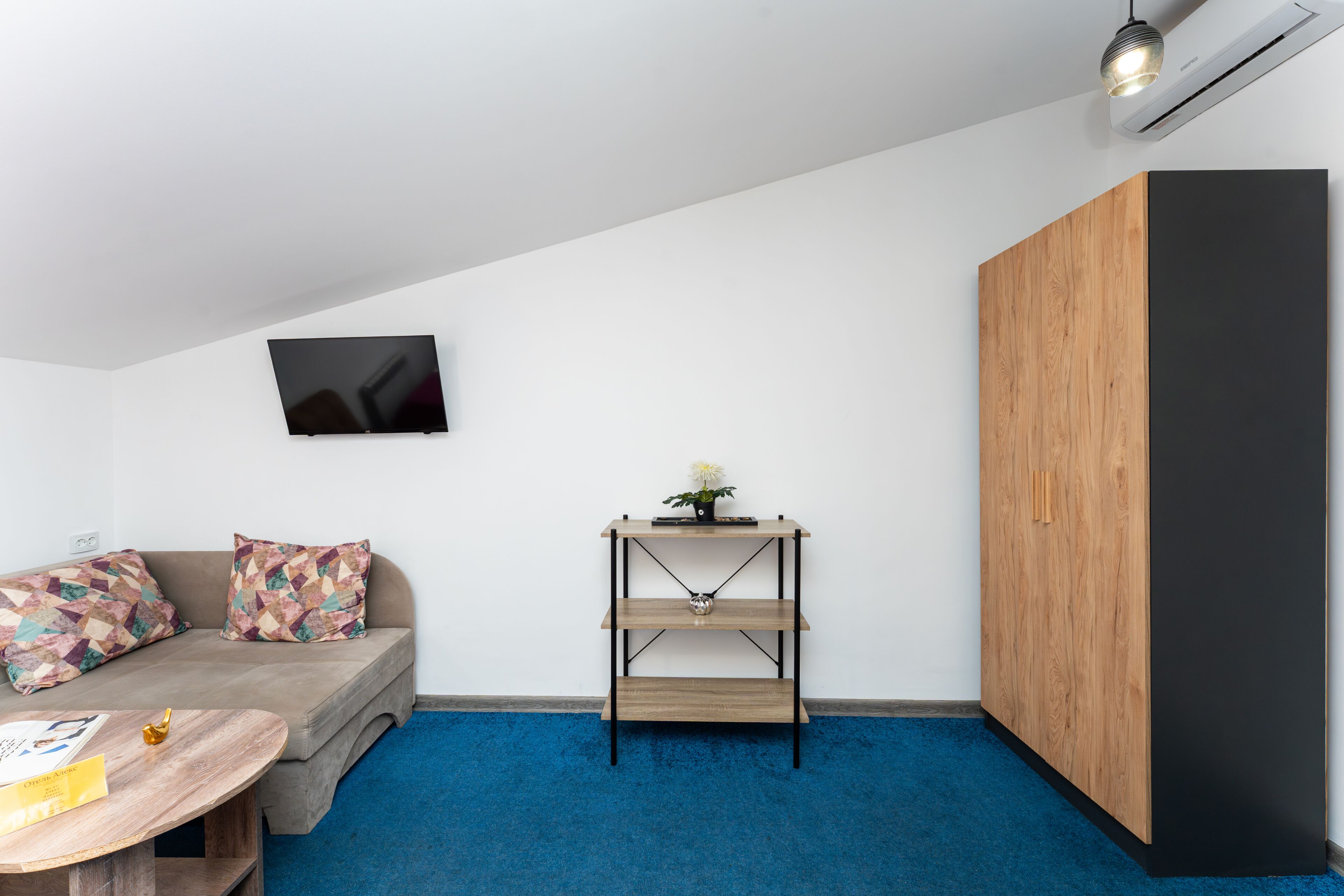 A modern room with a sofa, a small table, a wall-mounted TV, a wooden cabinet, and a blue carpet.