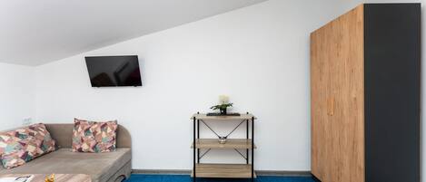 A modern room with a sofa, a small table, a wall-mounted TV, a wooden cabinet, and a blue carpet.