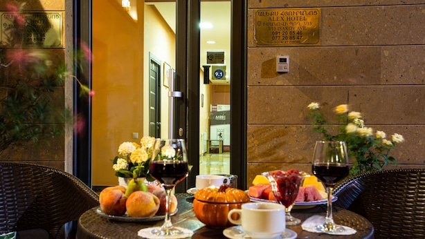 A table set with fruits, wine glasses, and a pumpkin centerpiece, indicating a dining area with a view of the hotel entrance. - Alex Hotel (Yerevan)