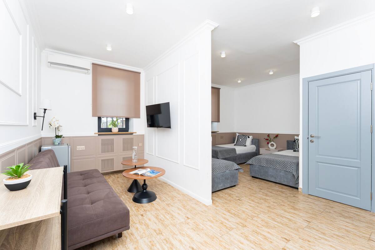 A modern apartment with a dining area, kitchenette, two bedrooms, a TV, and a door.