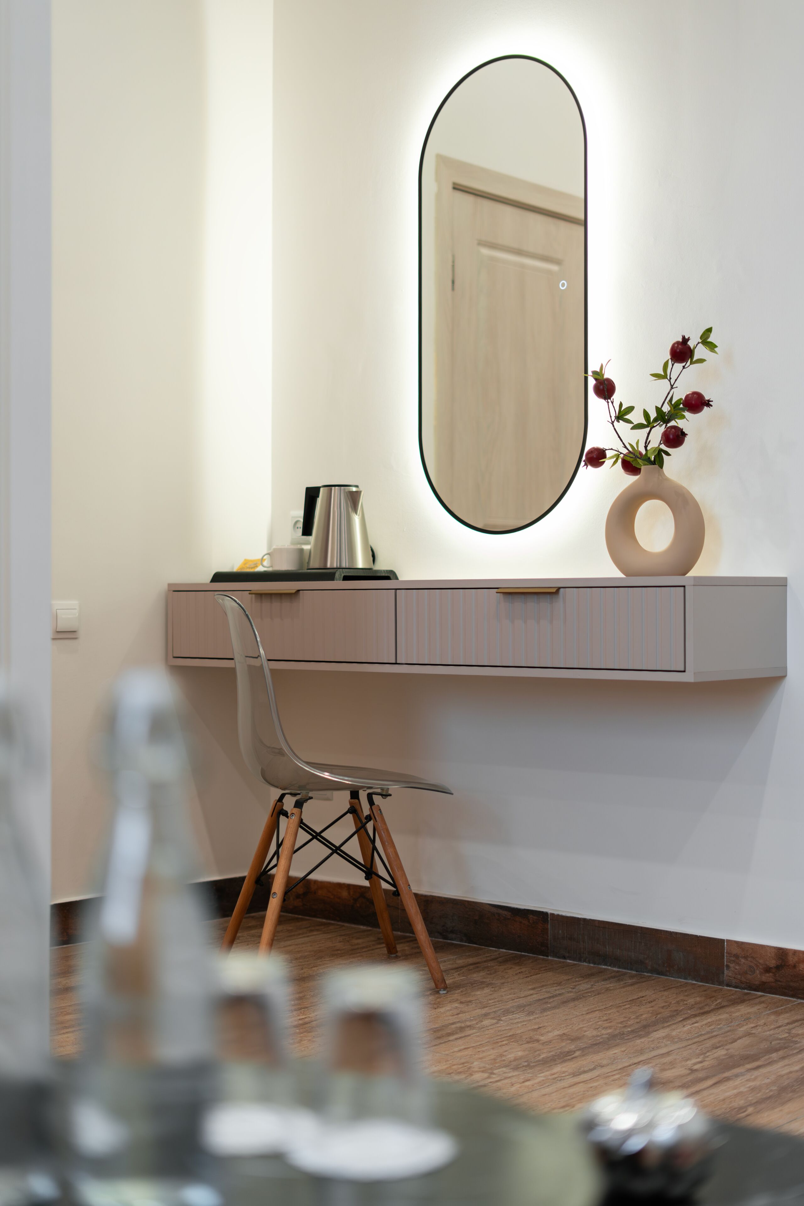 Ein modernes Zimmer mit Schreibtisch, Stuhl, Spiegel und einer Vase mit Blumen.