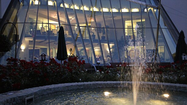 A modern building with a glass facade and a fountain in the foreground.