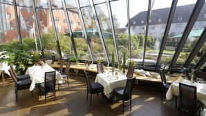 A restaurant with large glass windows, tables set with white tablecloths, and chairs.