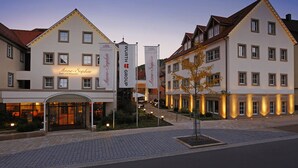 A hotel with a traditional European architectural style, featuring a central entrance with a glass canopy, multiple windows, and a well-lit facade.