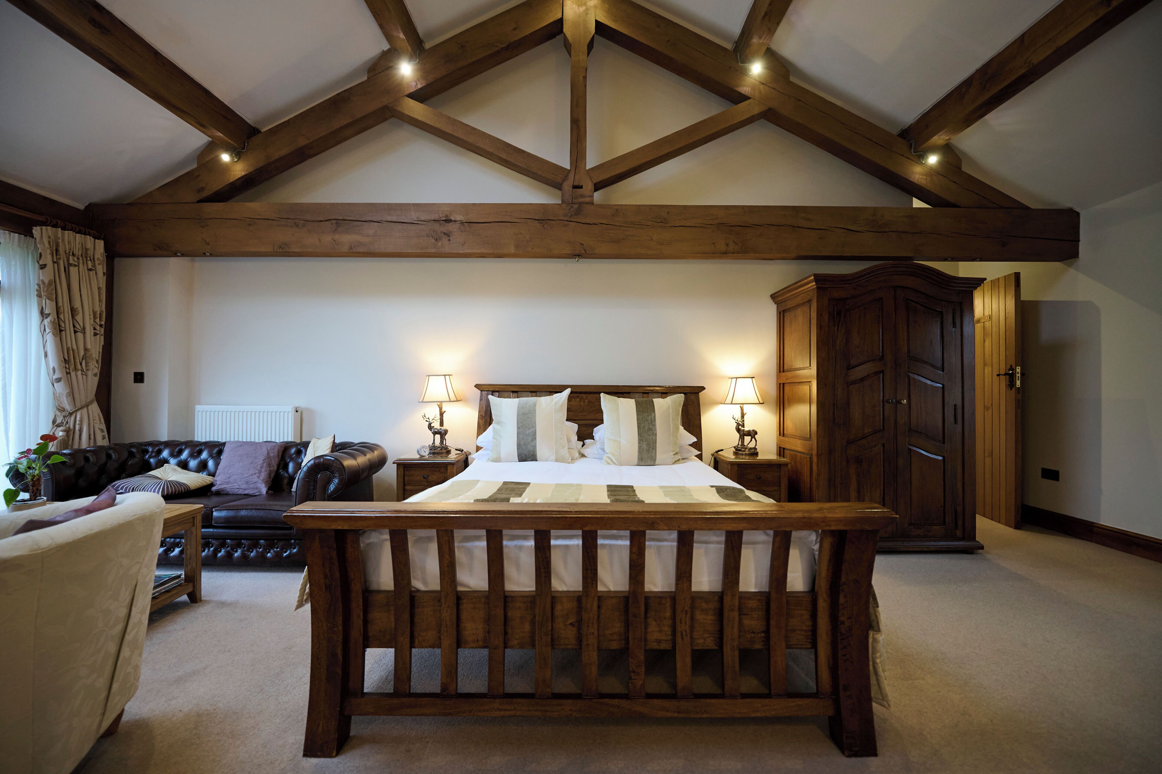 A bedroom with a wooden bed, a leather sofa, a wooden nightstand, and a wardrobe.