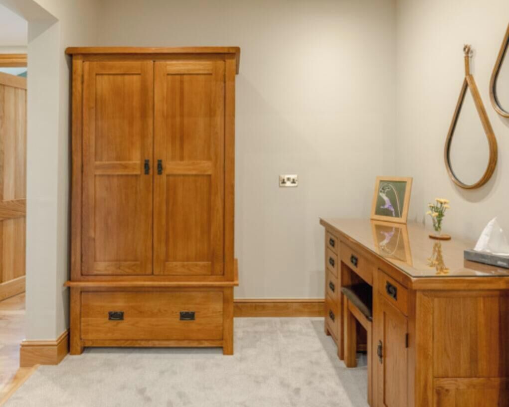 A room with a wooden wardrobe, a desk with drawers, a framed picture, and a hanging object on the wall.