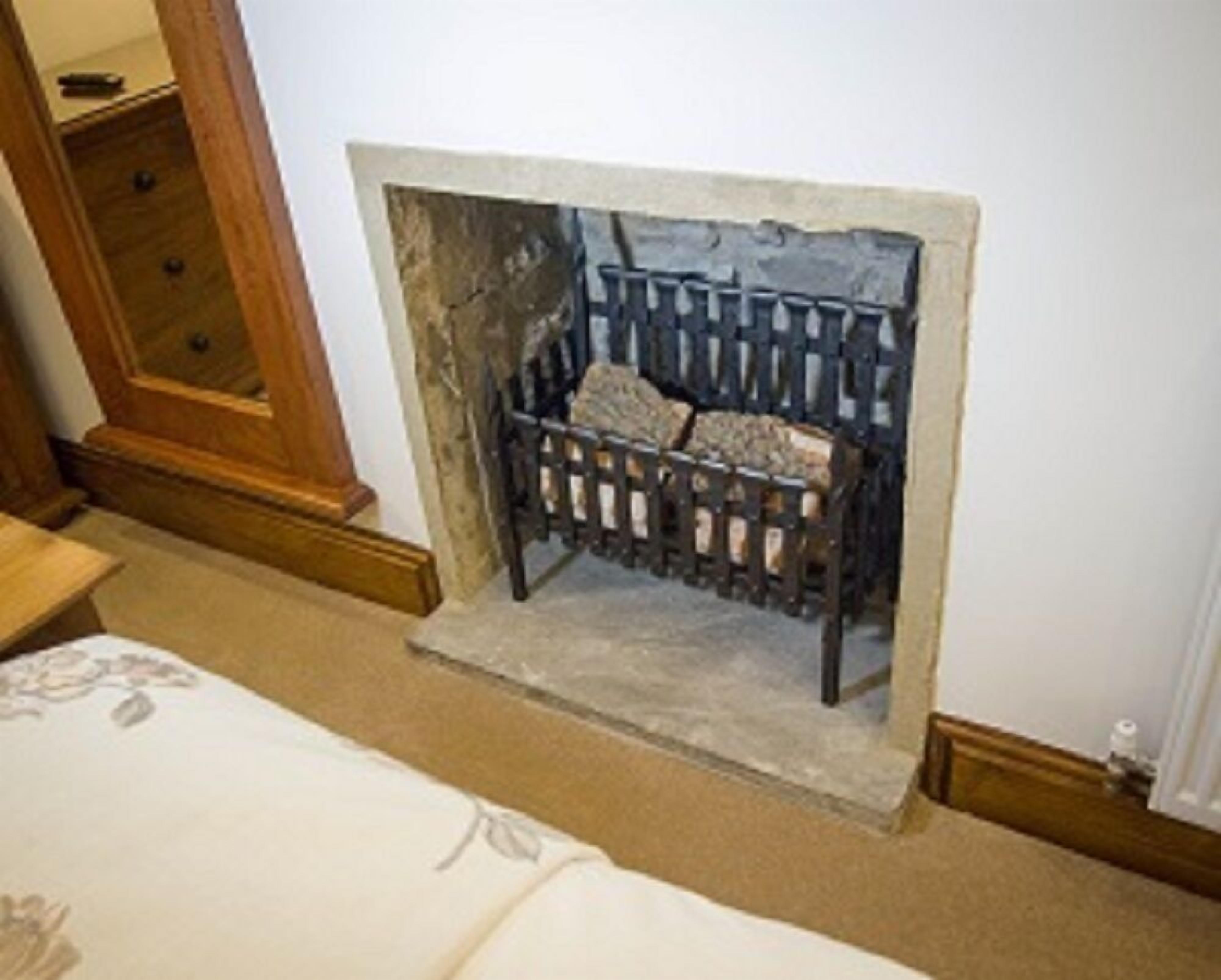 A room with a fireplace, a wooden dresser, and a bed with a floral bedspread.
